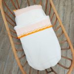 Parure bébé vintage en coton blanc avec dentelle et bordure orange, drap et taie d'oreiller en situation.