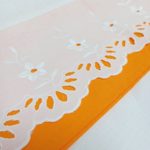 Détail de la dentelle et de la bordure orange sur le drap de lit et la taie d'oreiller.