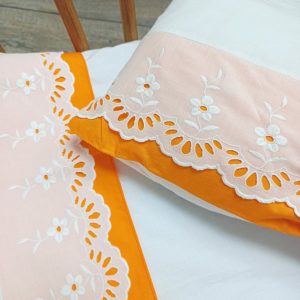 Détail de la bordure dentelle et orange sur le drap de lit et la taie